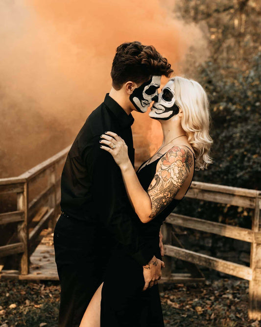 Skeleton-makeup couple kissing before orange smoke cloud