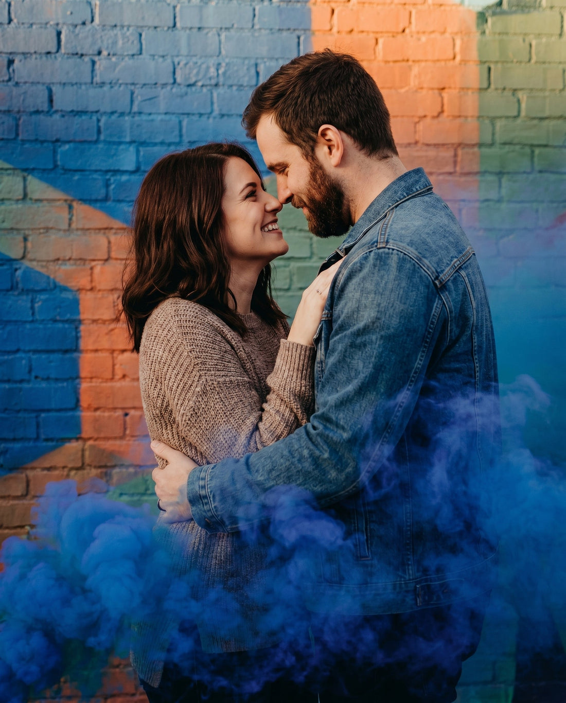 Person holding a blue smoke bomb against an urban brick wall, gripping the canister at the base