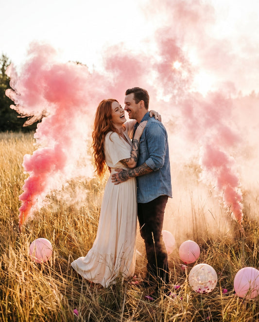 Pink smoke gender reveal in a grassy field at sunset