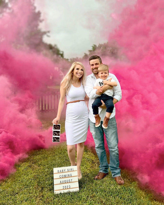 Pink non-toxic smoke drifting across a grassy backyard with a fence