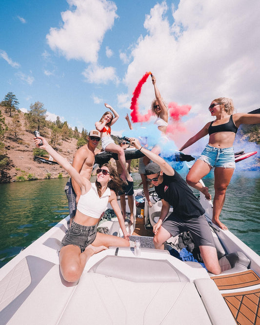 friends on a lake boat party trailing red and blue smoke over the water