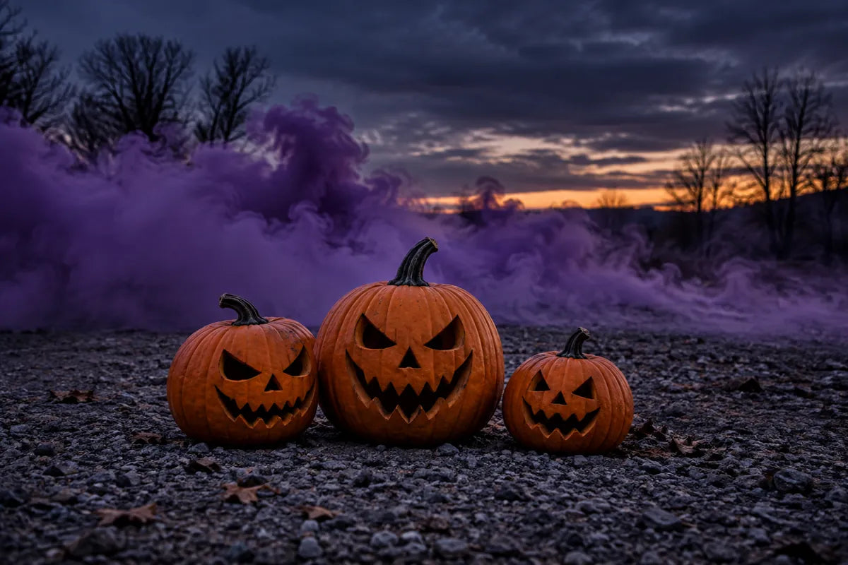Carved Halloween pumpkins on gravel with purple smoke in the background at dusk